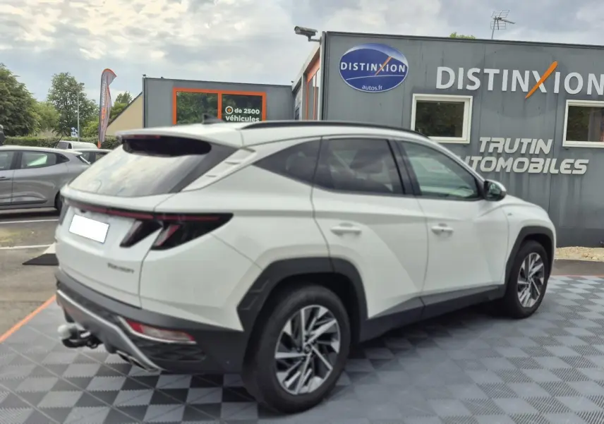 Vue 3/4 arrière droite d’un Hyundai Tucson blanc 2022 avec attelage, stationné devant un concessionnaire Distinxion.