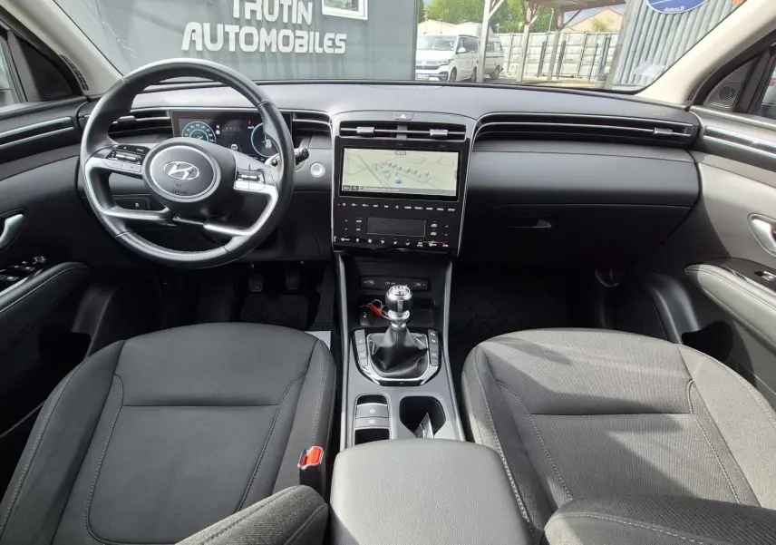 Vue intérieure frontale du Hyundai Tucson 2022, montrant le volant, la console centrale avec écran tactile et la boîte manuelle.