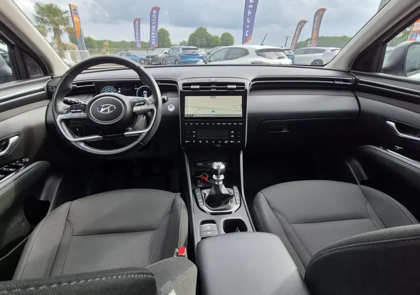 Vue intérieure avant du Hyundai Tucson 2022, montrant le volant, la console centrale avec boîte manuelle et les sièges en tissu noirs.