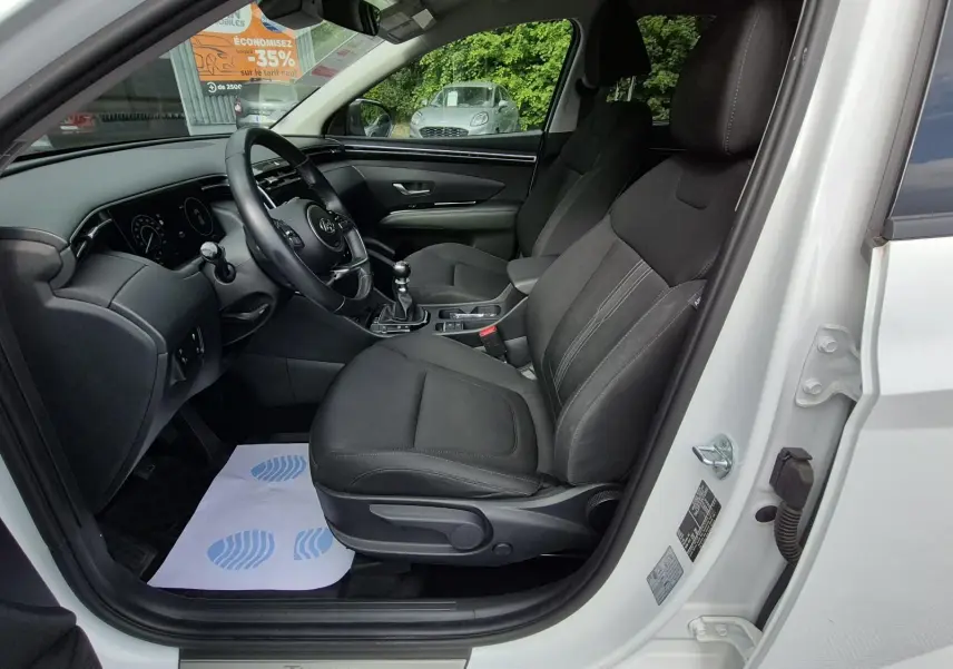 Vue intérieure côté conducteur du Hyundai Tucson blanc 2022, sièges tissu noirs et tableau de bord moderne.