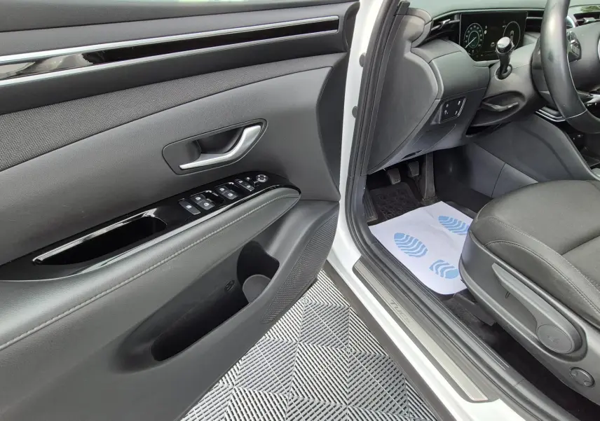 Vue intérieure côté conducteur du Hyundai Tucson blanc 2022, montrant la porte, siège tissu noir et tableau de bord.