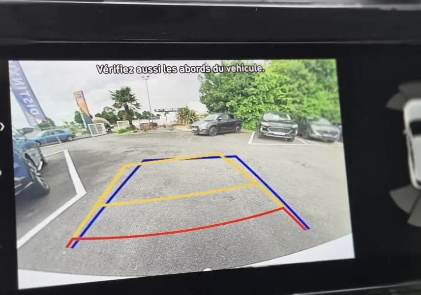Vue caméra de recul du Hyundai Tucson blanc 2022, avec lignes de guidage colorées sur un parking extérieur.