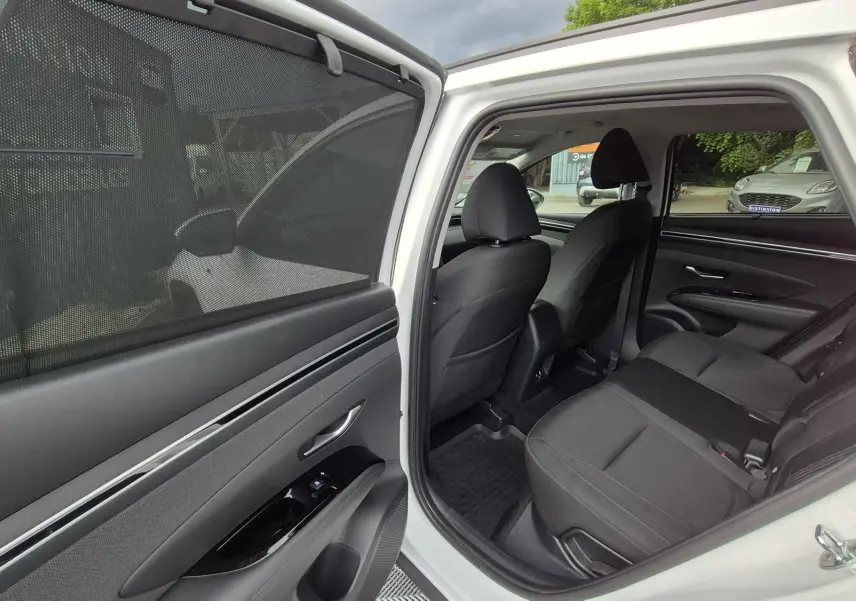 Vue intérieure côté arrière gauche d’un Hyundai Tucson blanc 2022, montrant les sièges arrière en tissu noir et la portière ouverte.
