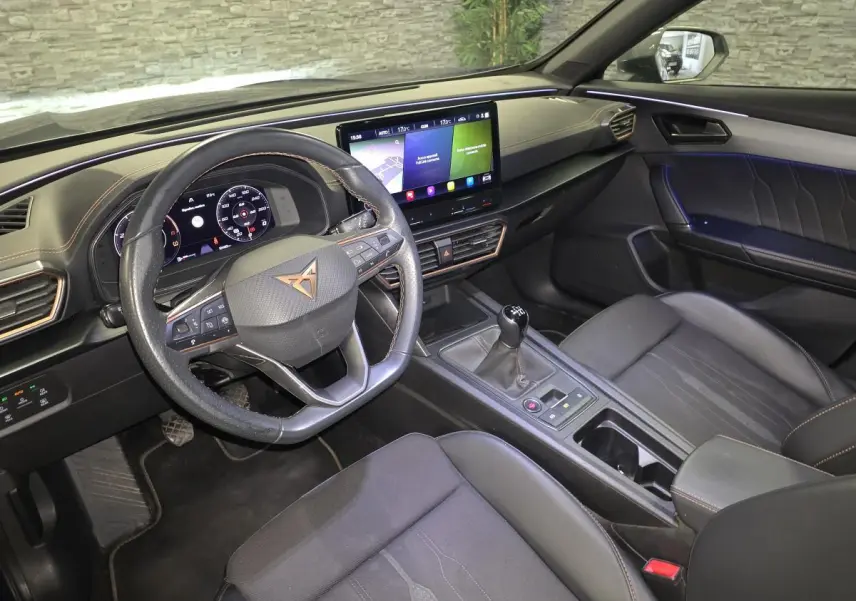 Vue intérieure côté conducteur du CUPRA Formentor 2023, tableau de bord noir avec volant sport, écran tactile et boîte manuelle.