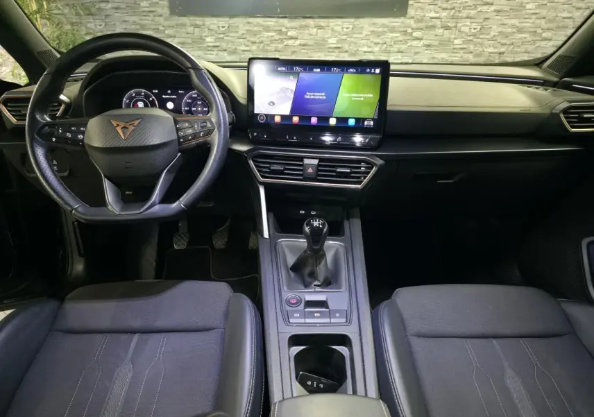 Vue intérieure frontale du tableau de bord et volant noir du CUPRA Formentor avec écran tactile et levier de vitesse manuel.