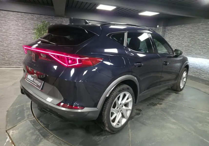 Vue 3/4 arrière droite du CUPRA Formentor bleu pétrole 2023 avec bandeau LED arrière 'Infinite Light' allumé.