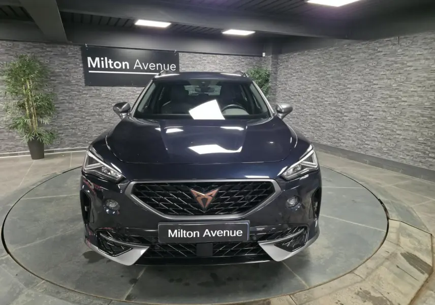 Vue avant d'un CUPRA Formentor bleu pétrole 2023 avec calandre noire et logo cuivre, dans un showroom intérieur.