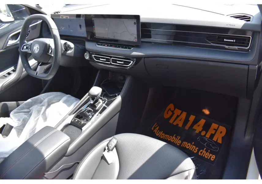Vue intérieure côté conducteur du MG MOTOR EHS 1.5 Hybrid+ 224 ch Luxury 2026, tableau de bord moderne avec écran large et volant multifonction.