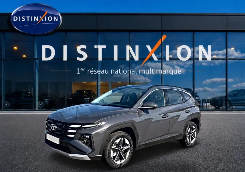Hyundai Tucson gris ecotonic en 3/4 avant droit, avec jantes alu et calandre distinctive, devant showroom Distinxion.