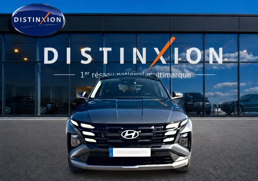 Vue avant d'un Hyundai Tucson gris ecotonic 2026 avec calandre noire distinctive et phares LED allumés.