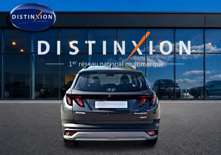 Vue arrière d'un Hyundai Tucson gris ecotonic hybride garé devant une vitrine Distinxion avec reflets de ciel.