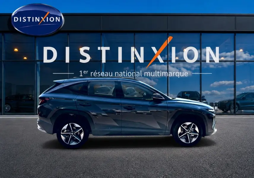 Vue de profil côté gauche d'un Hyundai Tucson gris ecotonic garé devant une vitrine avec logo Distinxion.