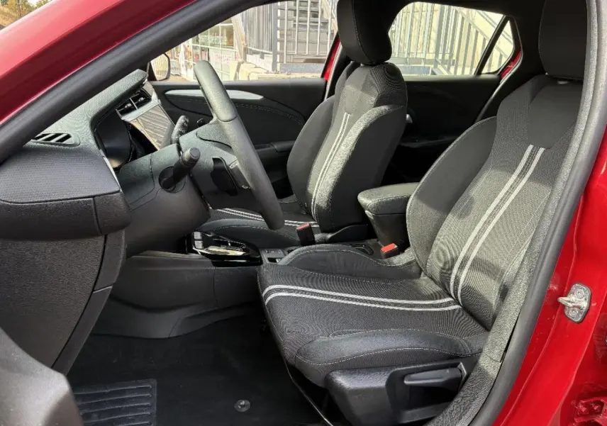 Vue intérieure côté conducteur de l’Opel Corsa 2025 rouge peperoncino, avec sièges noirs à bandes grises et tableau de bord moderne.