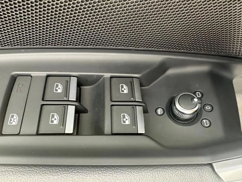 Gros plan sur les commandes des vitres électriques et réglages des rétroviseurs côté conducteur d'une Audi A3 Sportback 2024 noire.
