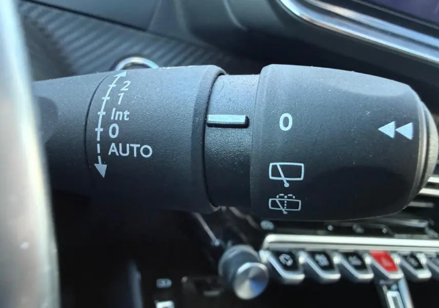 Gros plan sur la commande d’essuie-glace du Peugeot 208 Hybrid 110 e-DCS6 Allure noir, intérieur moderne avec boutons chromés.