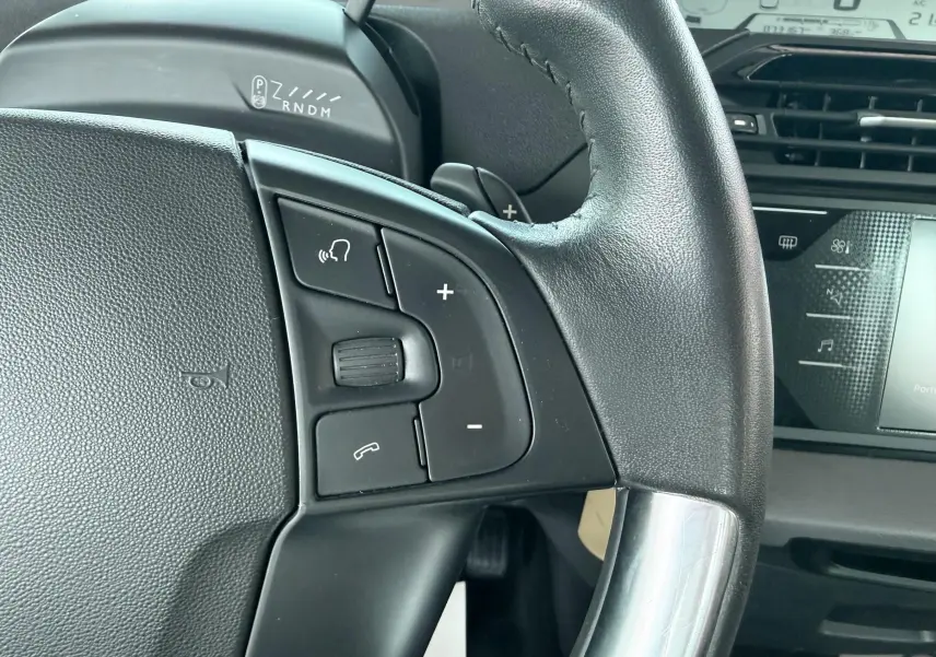 Gros plan sur le volant noir de la Citroën C4 Spacetourer 2019 avec commandes audio et tableau de bord numérique en arrière-plan.