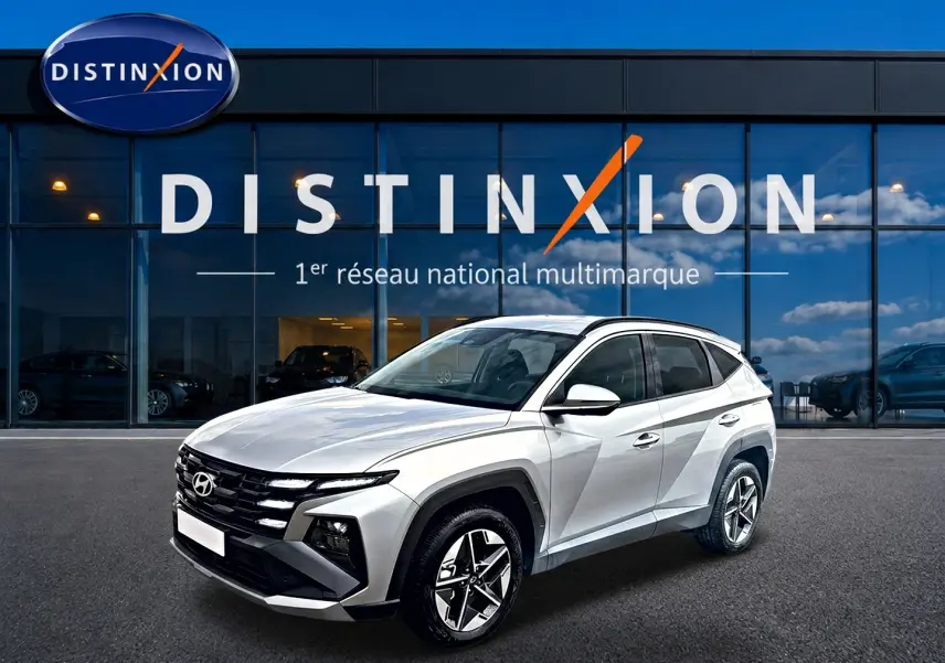 Hyundai Tucson gris shimmering en 3/4 avant droit, avec calandre noire et jantes alliage 18 pouces visibles.