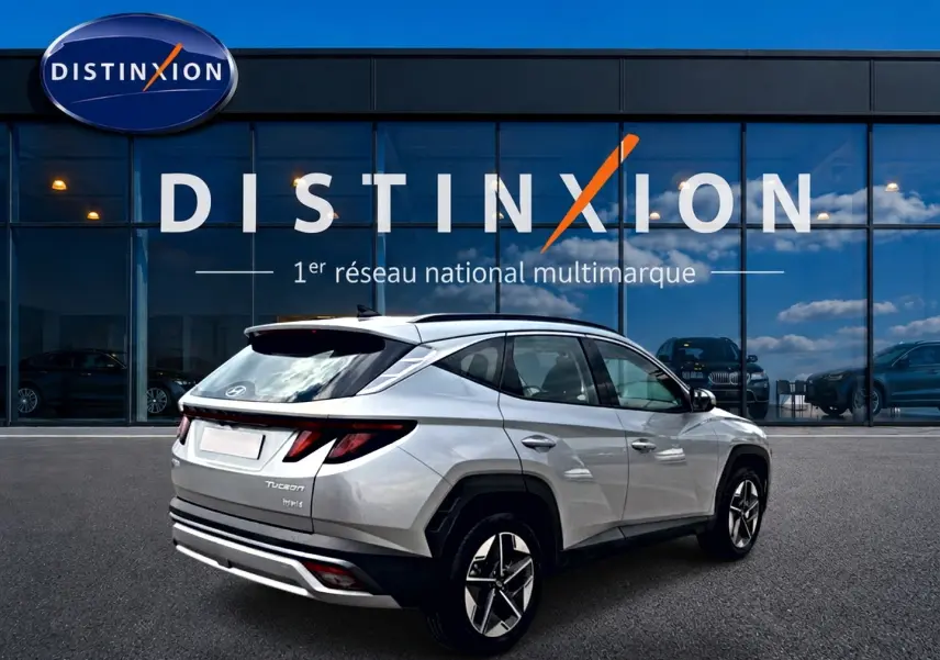 Hyundai Tucson gris shimmering en 3/4 arrière droit, avec feux LED et jantes alliage visibles devant vitrine Distinxion.