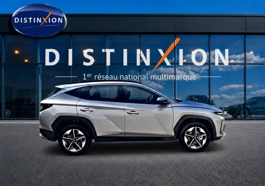 Vue latérale droite d'un Hyundai Tucson 2026 gris shimmering garé devant une vitrine avec logo Distinxion.