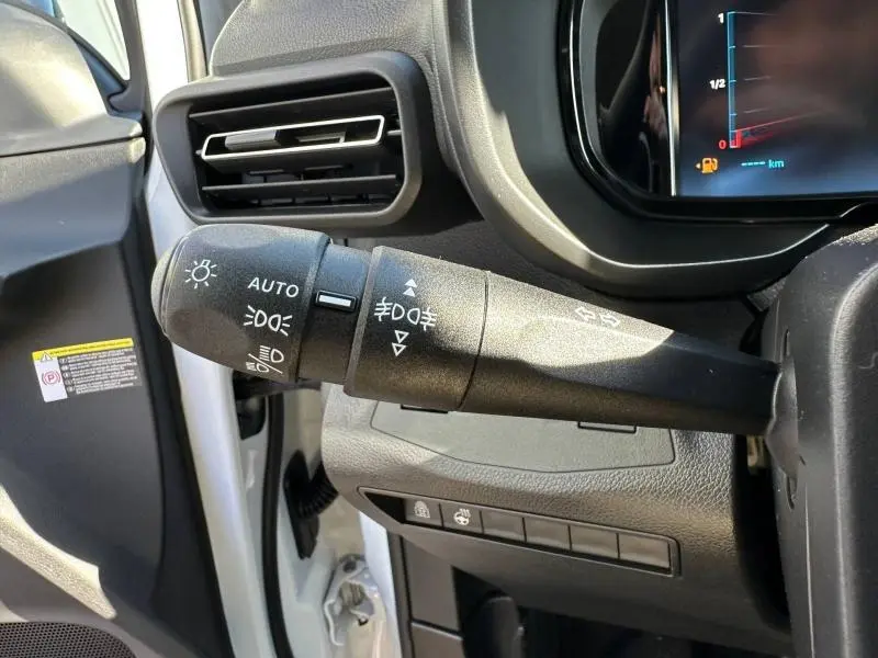 Gros plan sur la commande des phares à gauche du volant dans un Citroën Berlingo blanc, tableau de bord partiellement visible.
