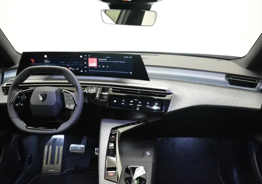 Vue intérieure avant du tableau de bord du Peugeot 3008 III Hybrid 145ch GT avec écran numérique panoramique et volant compact noir.