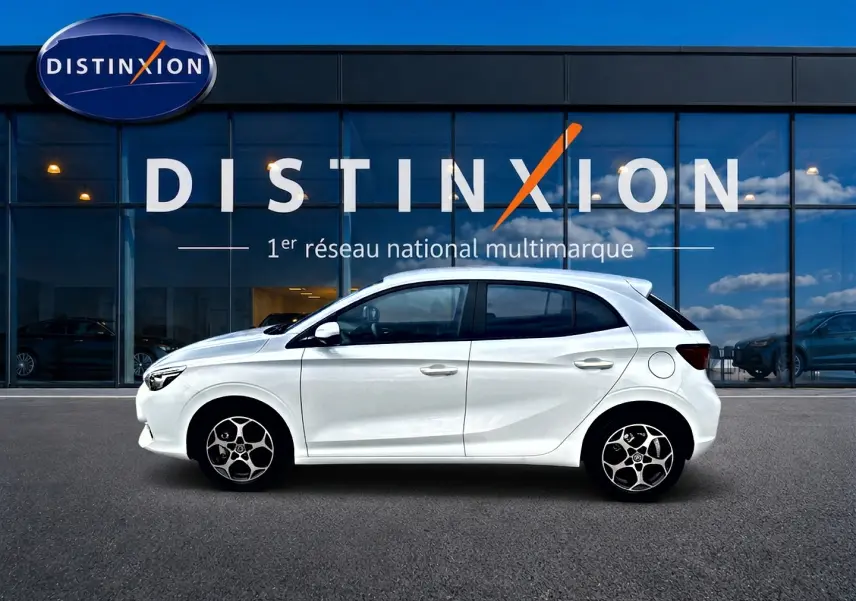 Profil droit d'une MG3 1.5 hybrid 195 luxury blanche, avec jantes alu et vitres teintées, devant une vitrine Distinxion.