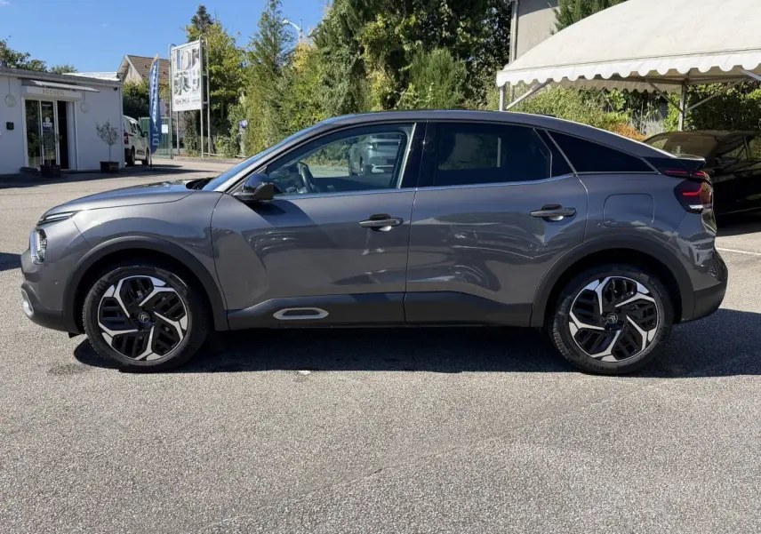 Vue de profil côté gauche d'une Citroën C4 PureTech 130 S&S Shine gris foncé, avec jantes distinctives et toit noir contrasté.