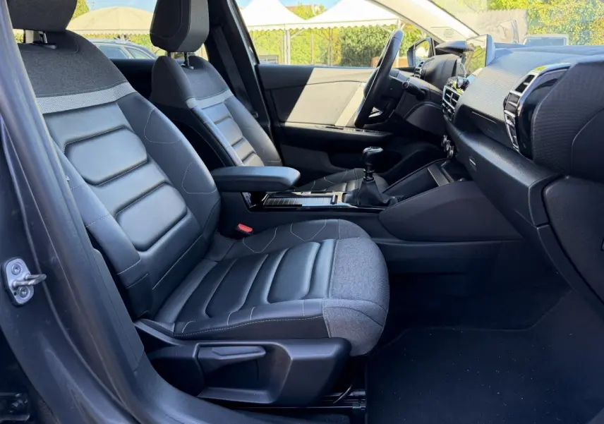 Vue intérieure côté conducteur de la Citroën C4 gris foncé, sièges bi-matière cuir et tissu, tableau de bord moderne.