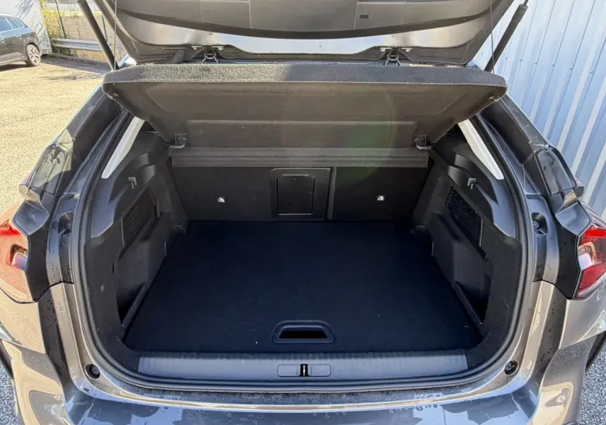 Coffre ouvert vu de l'arrière d'une Citroën C4 PureTech 130 S&S Shine gris foncé, espace de chargement vide.