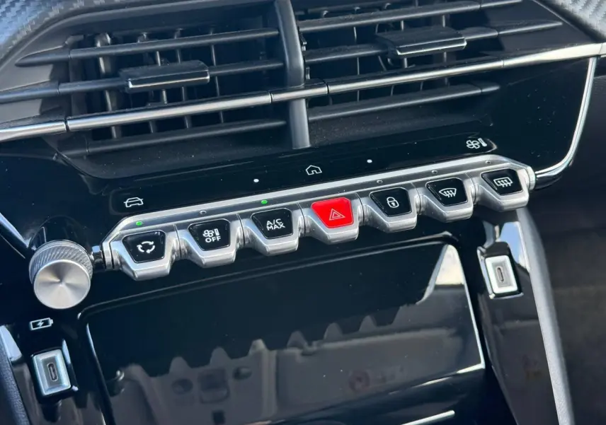 Gros plan sur la console centrale noire brillante du Peugeot 208 1.2 100ch Allure avec boutons argentés et rouge d’alerte.