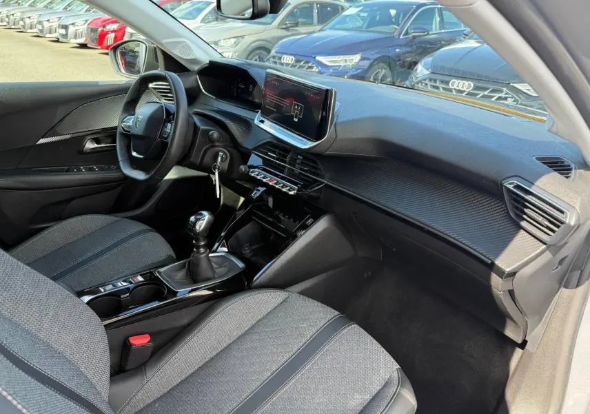 Intérieur avant droit de la Peugeot 208 1.2 100ch gris Artense, volant, écran tactile et levier de vitesse manuel visibles.