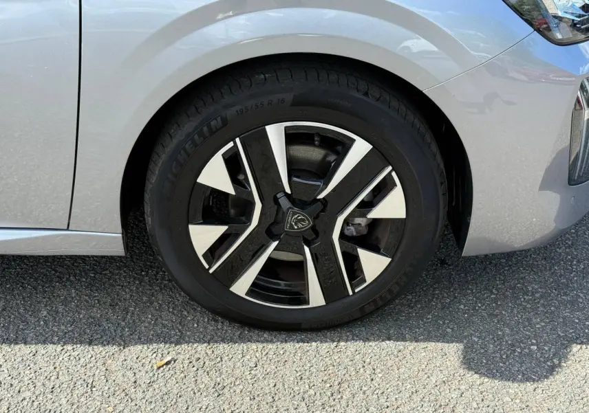 Gros plan sur la roue avant droite d’une Peugeot 208 gris Artense avec jante alu au design moderne.