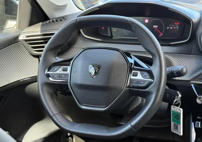 Vue rapprochée du volant Peugeot 208 1.2 100ch gris Artense, avec commandes intégrées et tableau de bord numérique.