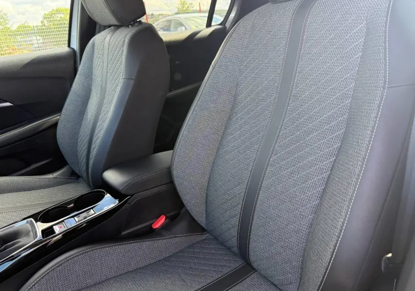 Vue rapprochée des sièges avant gris tissu et cuir avec accoudoir central et console brillante d'une Peugeot 208 2025.