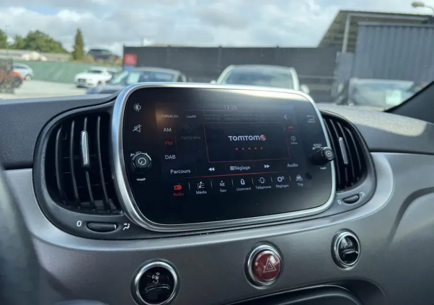 Écran tactile central 7'' avec interface TomTom sur tableau de bord gris satiné d'une Abarth 500 blanche, vue intérieure frontale.