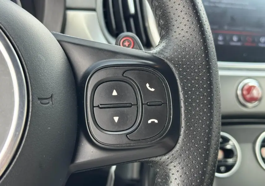 Gros plan sur les commandes noires du volant cuir perforé côté droit de l'Abarth 500 blanc, tableau de bord en arrière-plan.