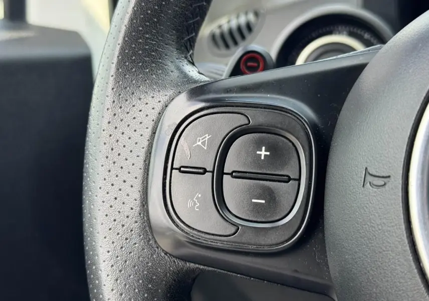 Gros plan sur les commandes de volume et de sourdine du volant cuir perforé de l'Abarth 500 blanc 2021.