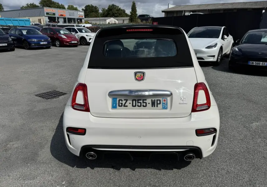 Vue arrière d'une ABARTH 500 blanche avec capote noire et double sortie d'échappement chromée sur parking.