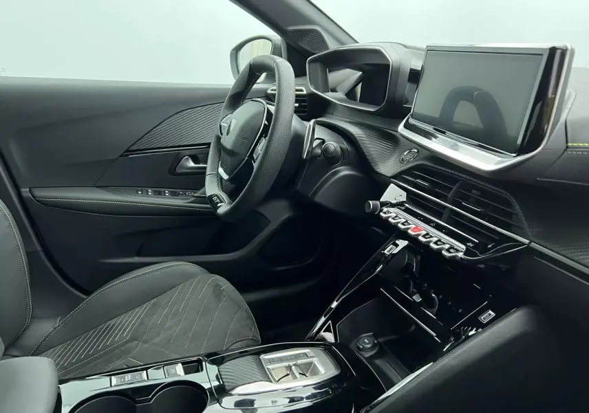 Vue intérieure côté conducteur de la Peugeot 208 1.2 Hybrid 136 GT 2025, avec tableau de bord noir et écran tactile central.