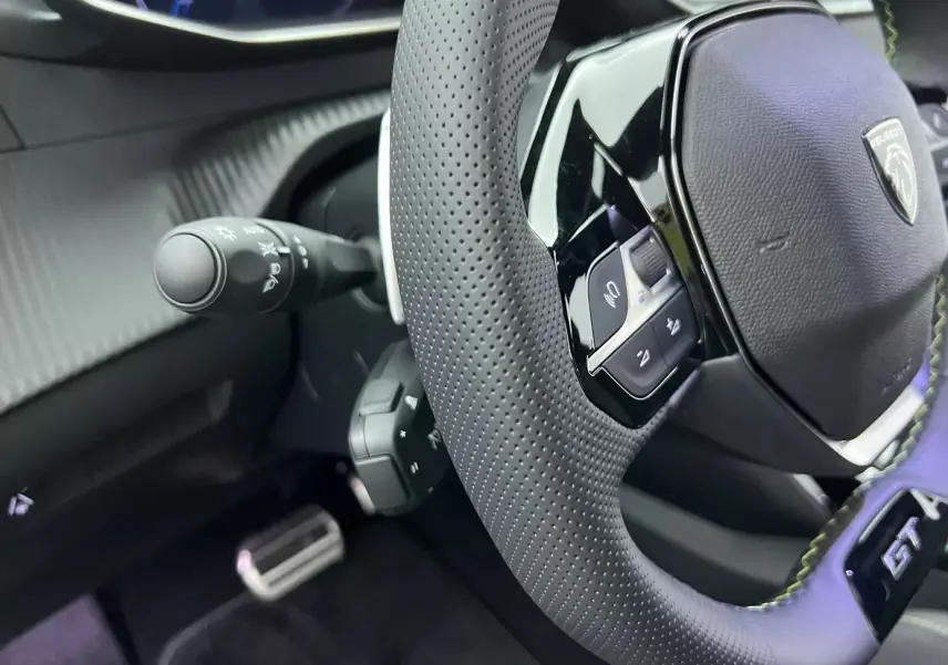 Gros plan sur le volant perforé noir avec logo Peugeot et badge GT de la Peugeot 208 1.2 Hybrid 136 blanche.