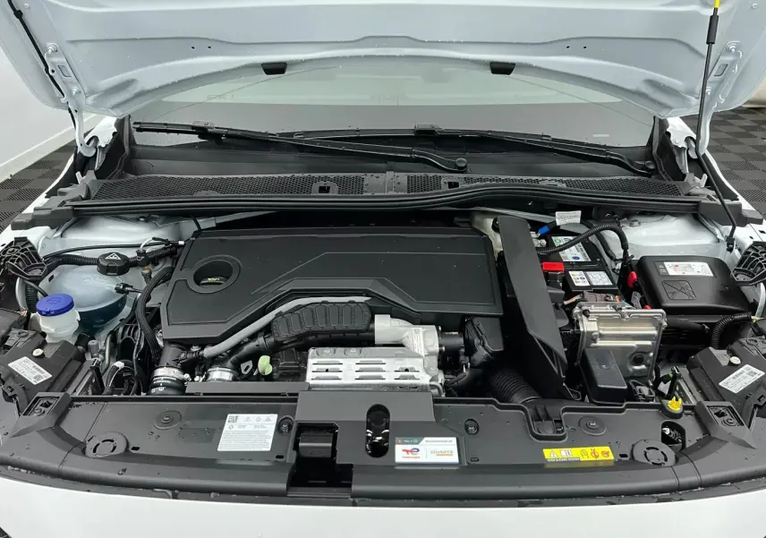 Moteur hybride Peugeot 208 1.2 HYBRID 136 GT blanc vu de face sous le capot ouvert, montrant le compartiment moteur.