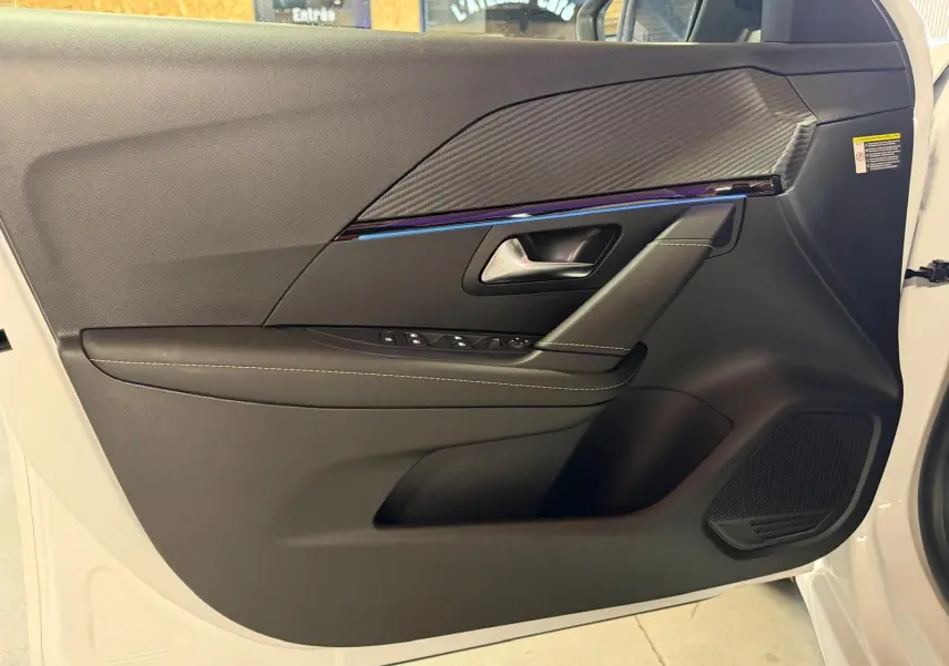 Vue intérieure du panneau de porte avant gauche noir avec surpiqûres et insert effet carbone sur Peugeot 208 blanc 2025.
