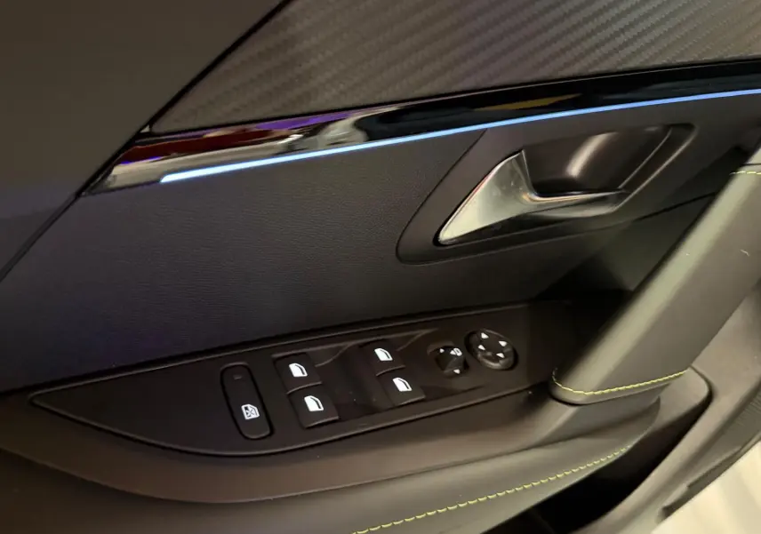 Détail de la porte côté gauche de la Peugeot 208 blanche 2025, montrant les commandes des vitres et la poignée intérieure.