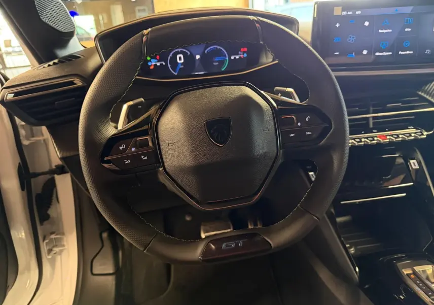 Vue intérieure centrée sur le volant noir GT et le tableau de bord numérique de la Peugeot 208 blanche 1.2 Hybrid 136.