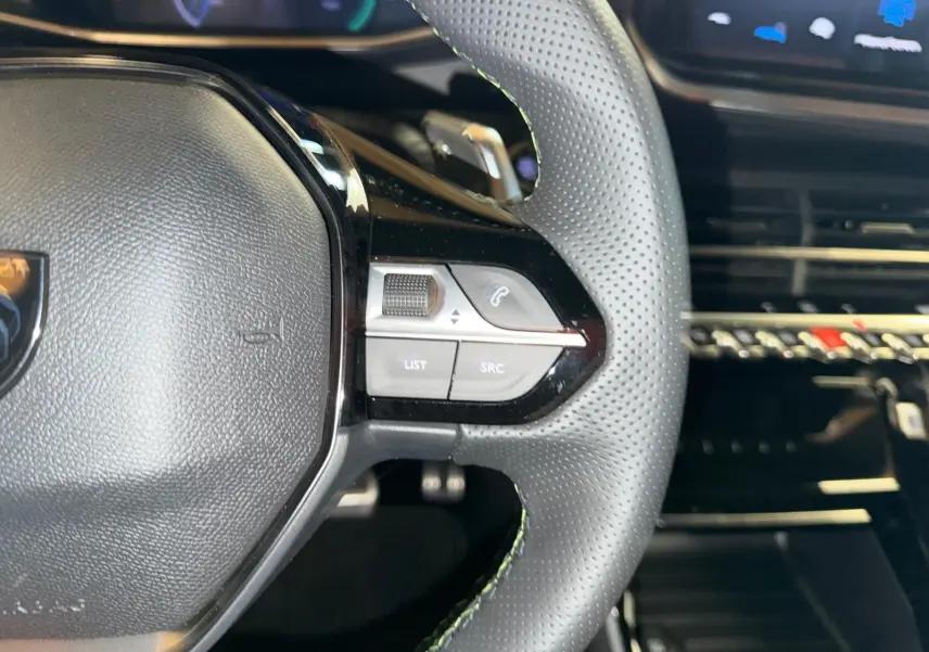 Gros plan sur le volant perforé de la Peugeot 208 1.2 HYBRID 136 GT avec commandes intégrées côté droit, intérieur noir.