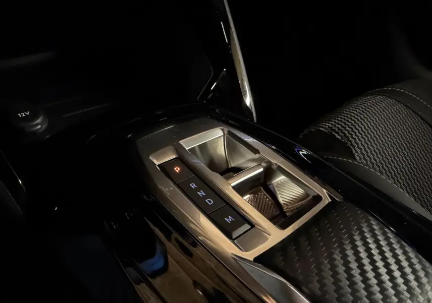 Gros plan sur la console centrale avec la boîte automatique de la Peugeot 208 1.2 Hybrid 136 GT, intérieur noir et détails carbone.
