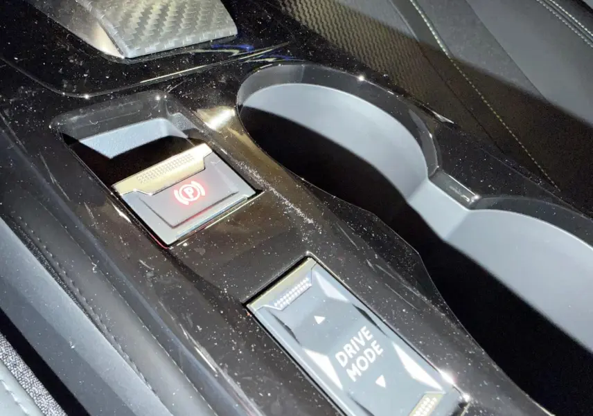 Gros plan sur la console centrale noire de la Peugeot 208 1.2 Hybrid 136 GT avec bouton frein à main électronique et sélection drive mode.