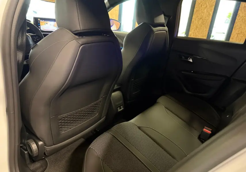 Vue intérieure arrière côté droit du Peugeot 208 1.2 Hybrid 136 GT blanc, sièges noirs en tissu et cuir avec surpiqûres.