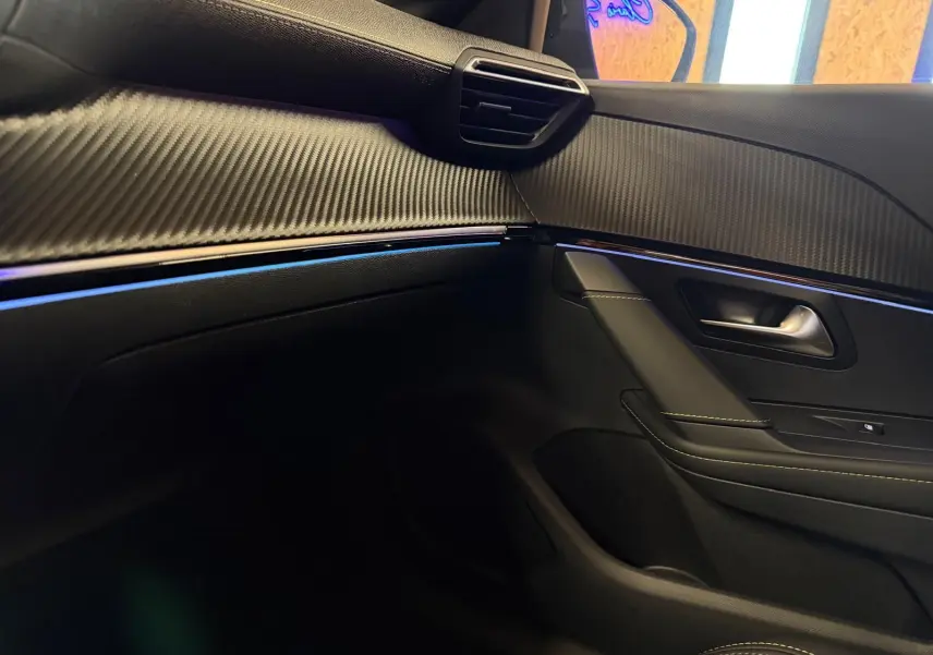 Détail de la porte côté passager de la Peugeot 208 1.2 Hybrid 136 GT 2025 en intérieur noir avec surpiqûres et insert effet carbone.