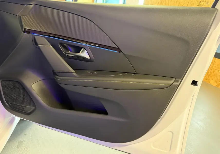 Vue intérieure côté gauche de la porte avant d’une Peugeot 208 1.2 Hybrid 136 GT blanche, avec garniture noire et surpiqûres contrastées.